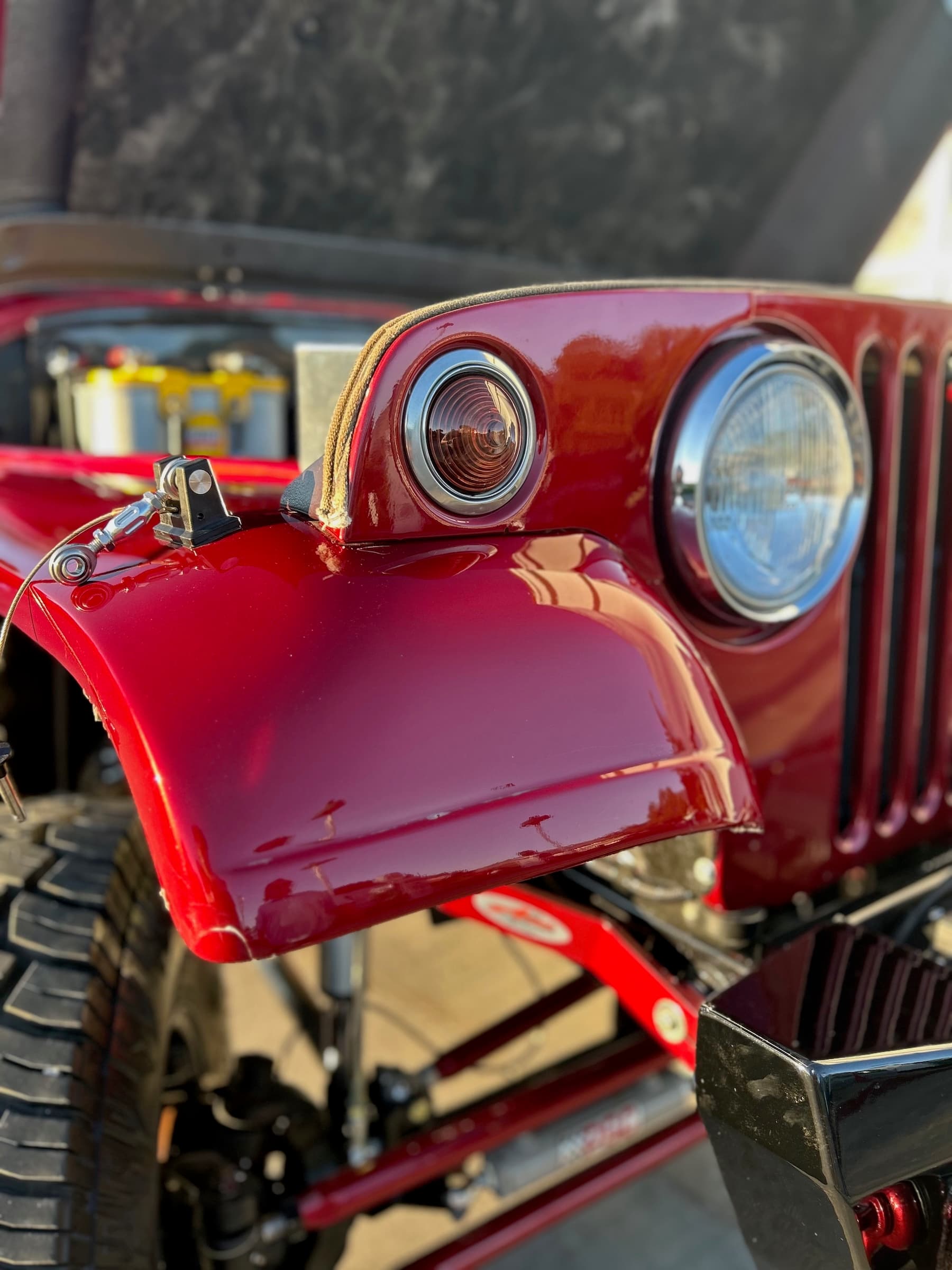 Close-up of a glossy red vintage Jeep's front fender, round headlight, and amber turn signal.