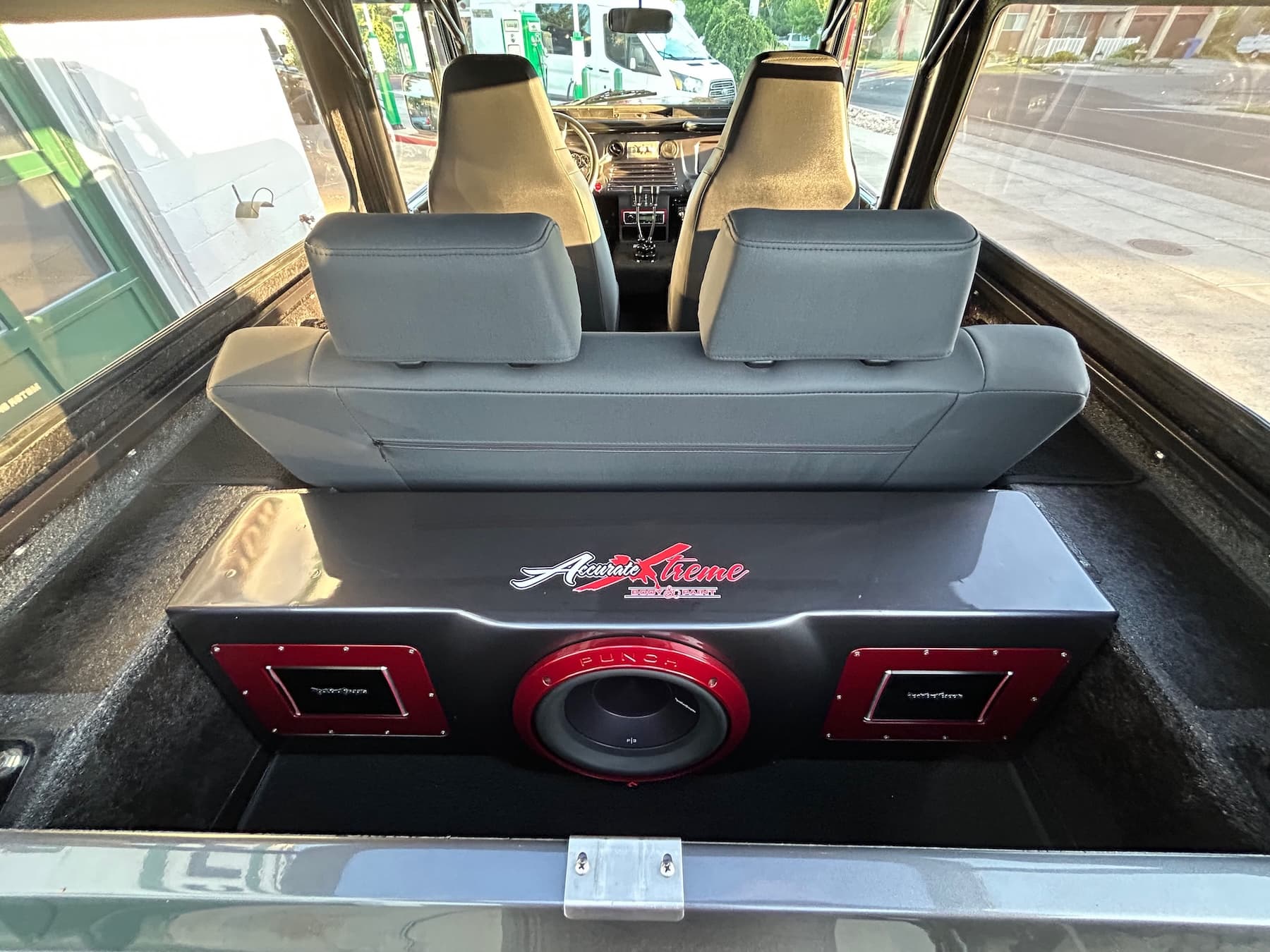 Custom Accurate Xtreme subwoofer box with red accents behind grey seats in a vehicle.