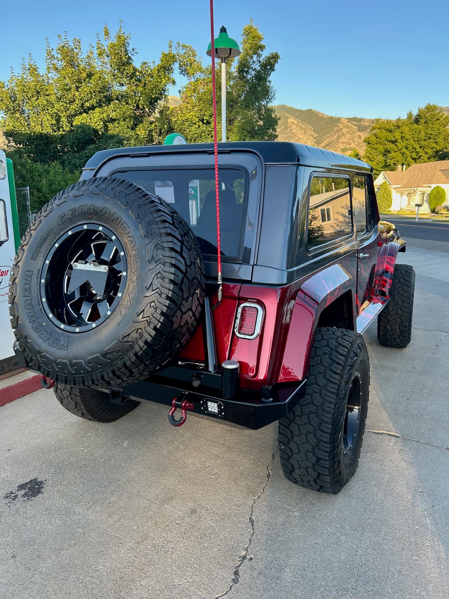 Red and black customized off-road vehicle with oversized tires and a rear-mounted spare tire.