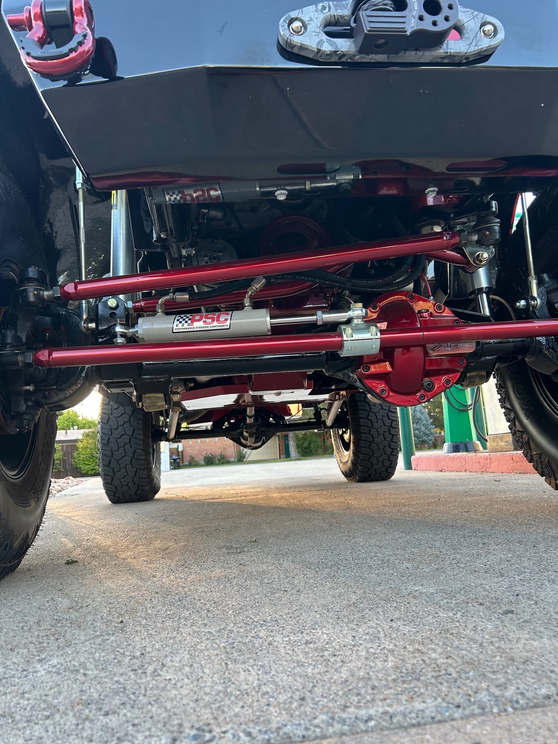 Undercarriage of a lifted vehicle showing red steering rods, differential cover, and PSC steering stabilizer.