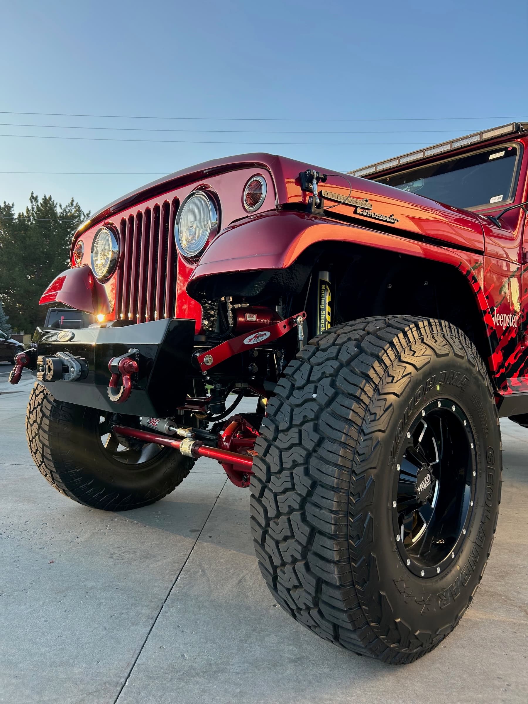 Modified red Jeepster Commando with massive off-road tires and custom suspension in the sunlight.